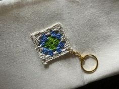 a crocheted square keychain with a green and blue flower on it