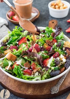 a salad with strawberries, lettuce and nuts being drizzled with dressing