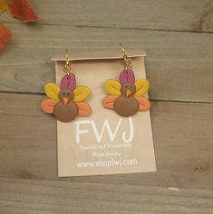 a pair of earrings with turkeys on them sitting on top of a wooden table