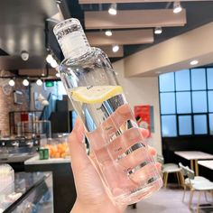 a person holding up a glass bottle filled with water and lemons in front of a counter