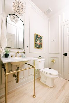 a white toilet sitting next to a sink in a bathroom under a mirror and gold faucet