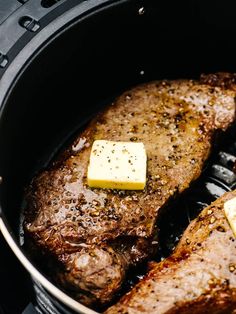 two steaks cooking in an air fryer with butter and seasoning on them