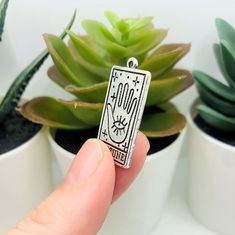 a person is holding up a small pendant with the word boo on it in front of some succulents