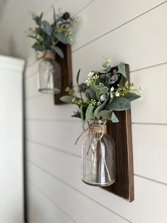 two mason jars with greenery are hanging on the side of a white house wall