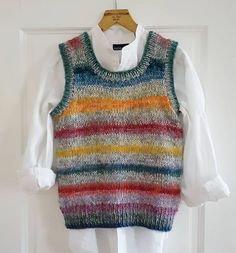 a multicolored sweater vest hanging on a door hanger with a white shirt underneath it