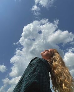 a woman looking up into the sky with her head tilted to the side and clouds in the background