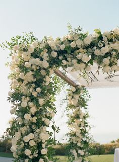 an outdoor wedding ceremony with white flowers and greenery on the arch over the aisle