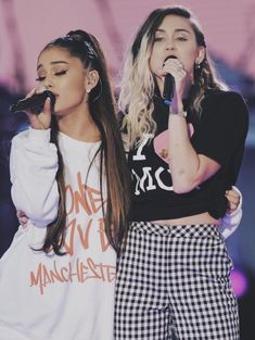 two girls standing next to each other on stage with microphones in their hands and one holding