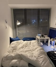 an unmade bed with white sheets and pillows in a bedroom next to a window