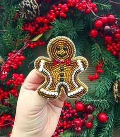 a hand holding a beaded ginger ornament in front of a christmas wreath