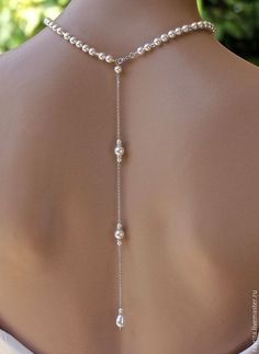 the back of a woman's neck wearing a white necklace with pearls on it