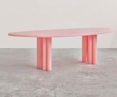 a pink table sitting on top of a cement floor next to a white wall with columns