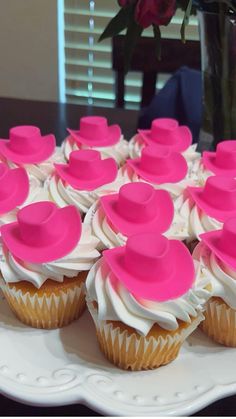 cupcakes with white frosting and pink hats on them are arranged on a plate