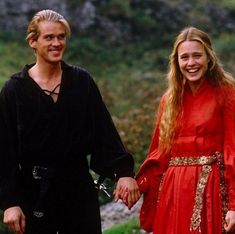 a man and woman dressed in medieval clothing holding hands while standing next to each other