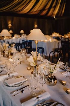 a table set with silverware and white flowers in vases on top of it