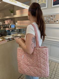 a woman holding a pink flowered bag in front of a bakery