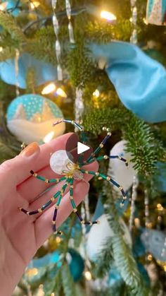 a hand holding a spider ornament in front of a christmas tree with ornaments