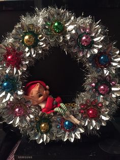 a christmas wreath with an elf doll in the center and other ornaments around it on a table