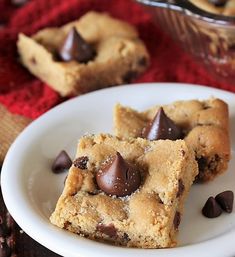 two pieces of chocolate chip cookie on a white plate next to a bowl of cookies