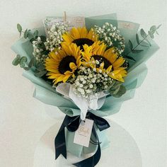 a bouquet of sunflowers and baby's breath wrapped in blue ribbon on a table