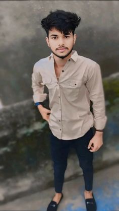 a young man with black hair standing in front of a wall and looking at the camera