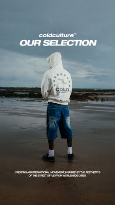 a man standing on top of a sandy beach next to the ocean wearing a white hoodie