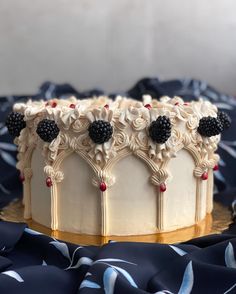 a cake with white frosting and blackberries on top sitting on a blue cloth