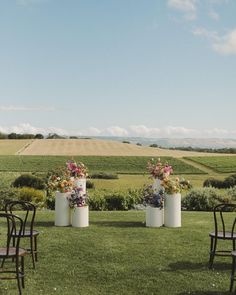 two tall vases with flowers are sitting in the grass near some chairs and tables