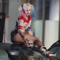 a woman with colorful hair sitting on the hood of a car wearing fishnet stockings