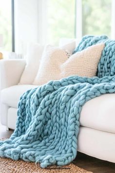 a white couch with a blue knitted blanket on it's back in front of a window