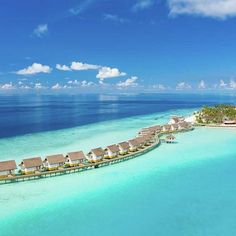 an aerial view of a resort over the water with thatched huts on stilts