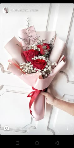 a person holding a bouquet of flowers in their hand on a white door with red ribbon