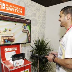 a man standing in front of a nintendo wii game system playing mario kart on the nintendo switch