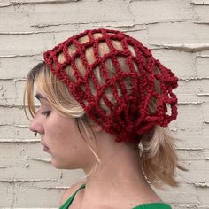 a woman wearing a red knitted hat with braids on her head, against a white brick wall