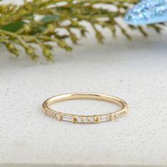 a yellow gold ring with five small diamonds on the side, sitting next to a plant