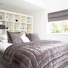 a large bed sitting under a window next to a white book shelf filled with books