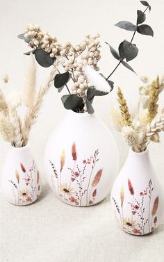 two white vases with flowers and plants in them