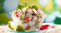 a salad in a glass bowl with limes, tomatoes and other vegetables on the side