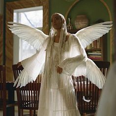 a woman dressed in white with large wings and beaded necklaces on her head