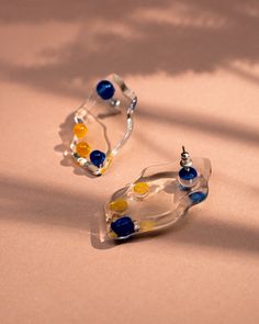 two clear earrings with blue, yellow and white beads are on a light pink surface