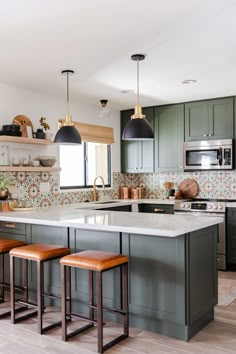 a kitchen with green cabinets and wooden stools in front of the countertop area