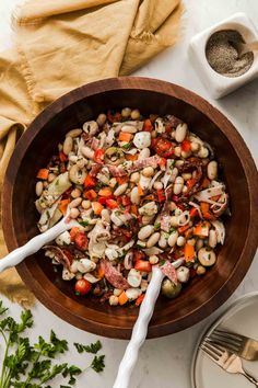 a wooden bowl filled with beans and vegetables next to a white spoon on top of a table