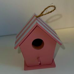 a pink birdhouse on a white table with a brown string hanging from it's roof