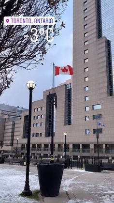 the canadian flag is flying in front of a large building with tall windows and snow on the ground