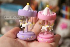 two small toy carousels in the palm of a person's hand, one pink and one purple