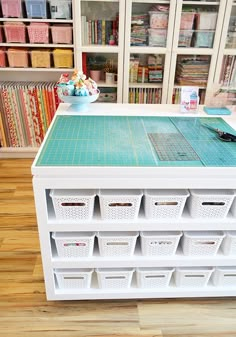 a sewing table with several baskets on it and bookshelves in the back ground