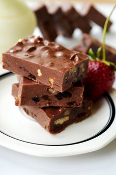 three pieces of chocolate fudge on a plate with a strawberry and milk in the background