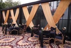 an outdoor event with black tables and gold drapes