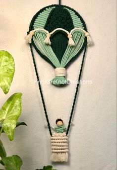 a green and white hot air balloon hanging on a wall next to a plant with leaves