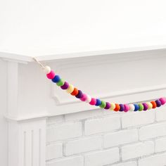 a colorful garland hanging from a fireplace mantel in front of a white brick wall